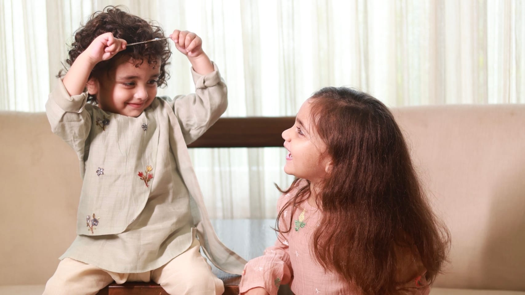 Two children in hand-embroidered kachche dhaage kurta sets, sitting together on a low wooden table