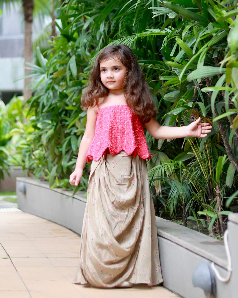 The coral top's scalloped hem and the sage skirt's drape, against greenery