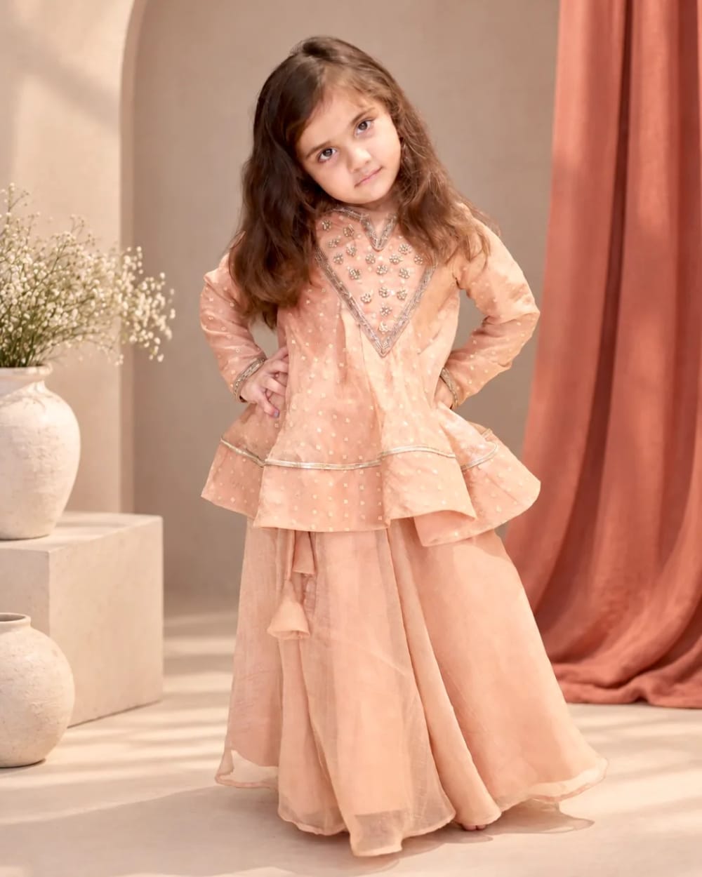 A girl in a peach peplum kurta with an embroidered yoke, over a matching sharara
