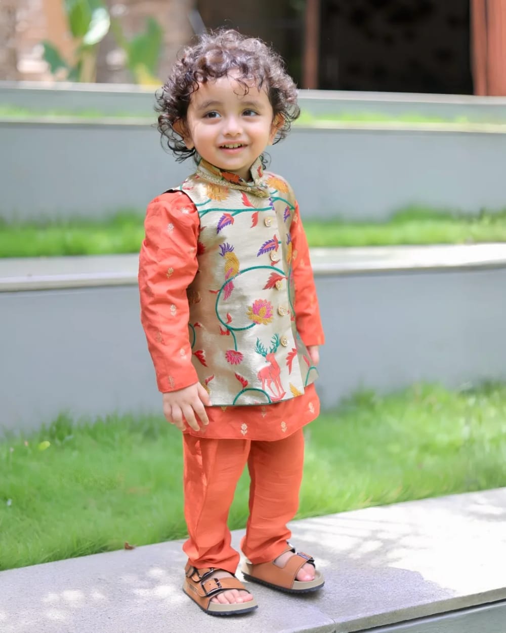 A child in a coral kurta set under a painted sage jacket