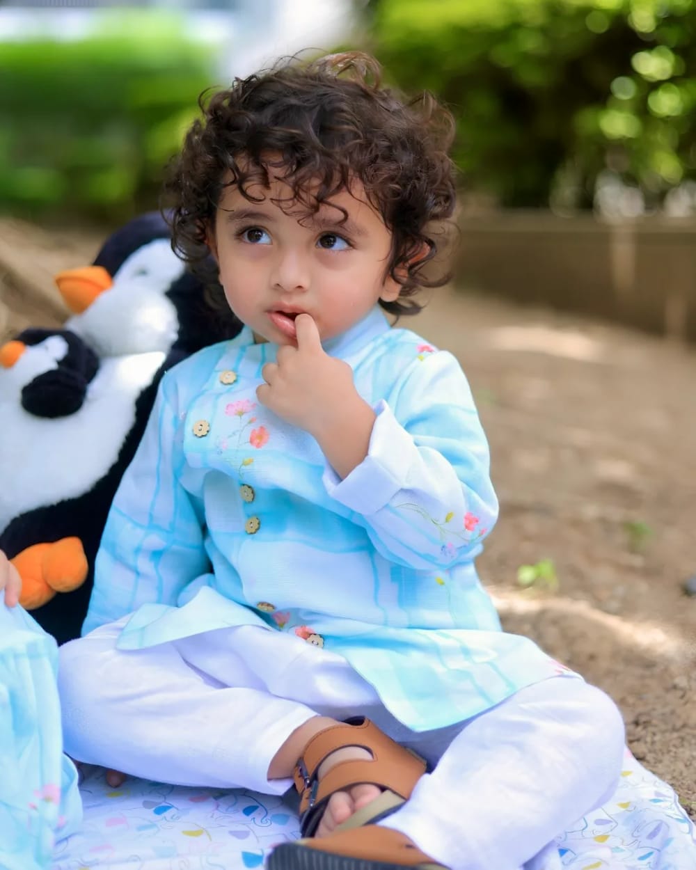 A child in a pale blue kurta with gold buttons, sitting on a picnic blanket