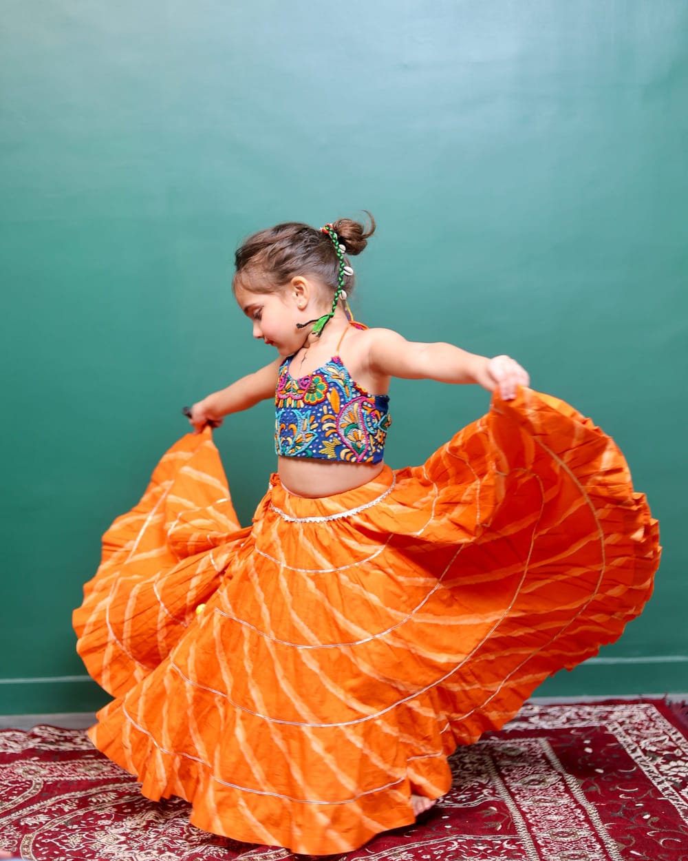 A girl mid-twirl in an orange leheriya ghagra, the skirt lifted into a full circle