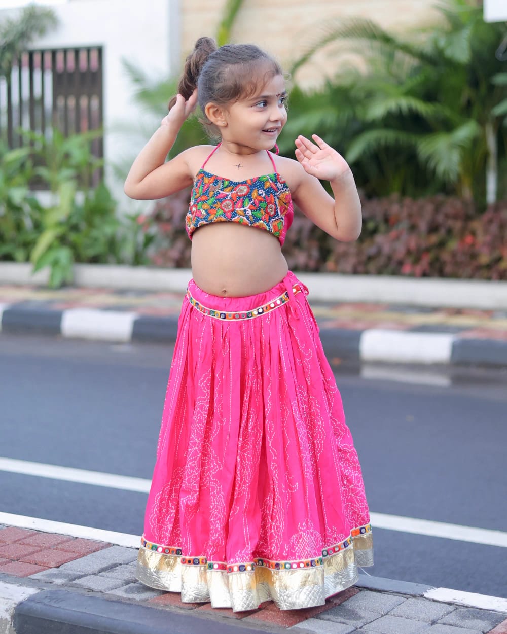 A girl in a pink bandhani chaniya choli at the roadside, the skirt falling full to her feet