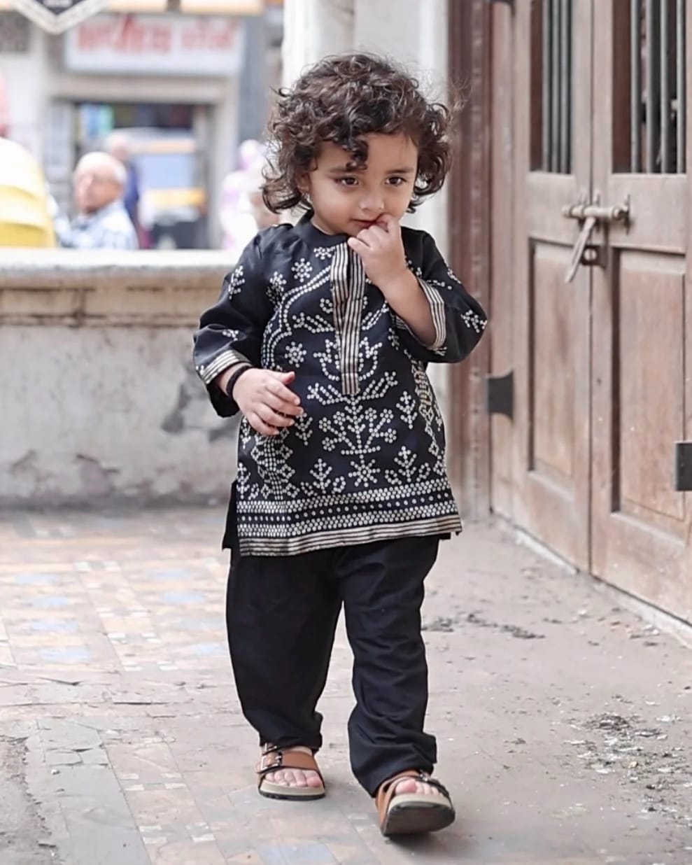 A small boy walking down a lane in a black bandhani kurta and pyjama