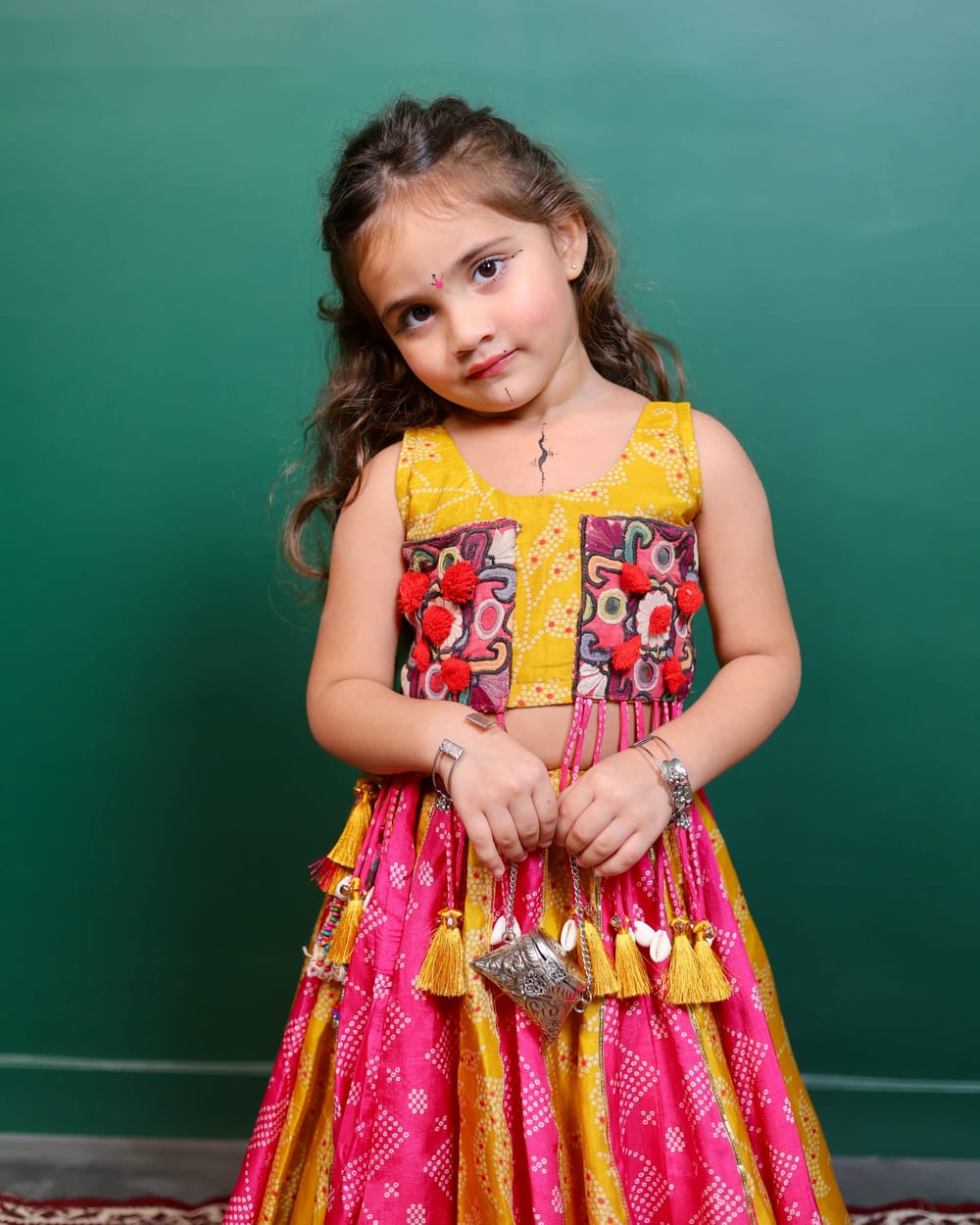 A girl in a pink and mustard bandhani ghagra with a hand-embroidered yellow choli