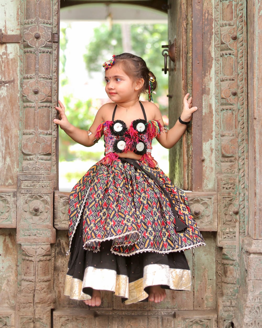 A girl standing in a carved doorway, the ikat skirt swinging out around her